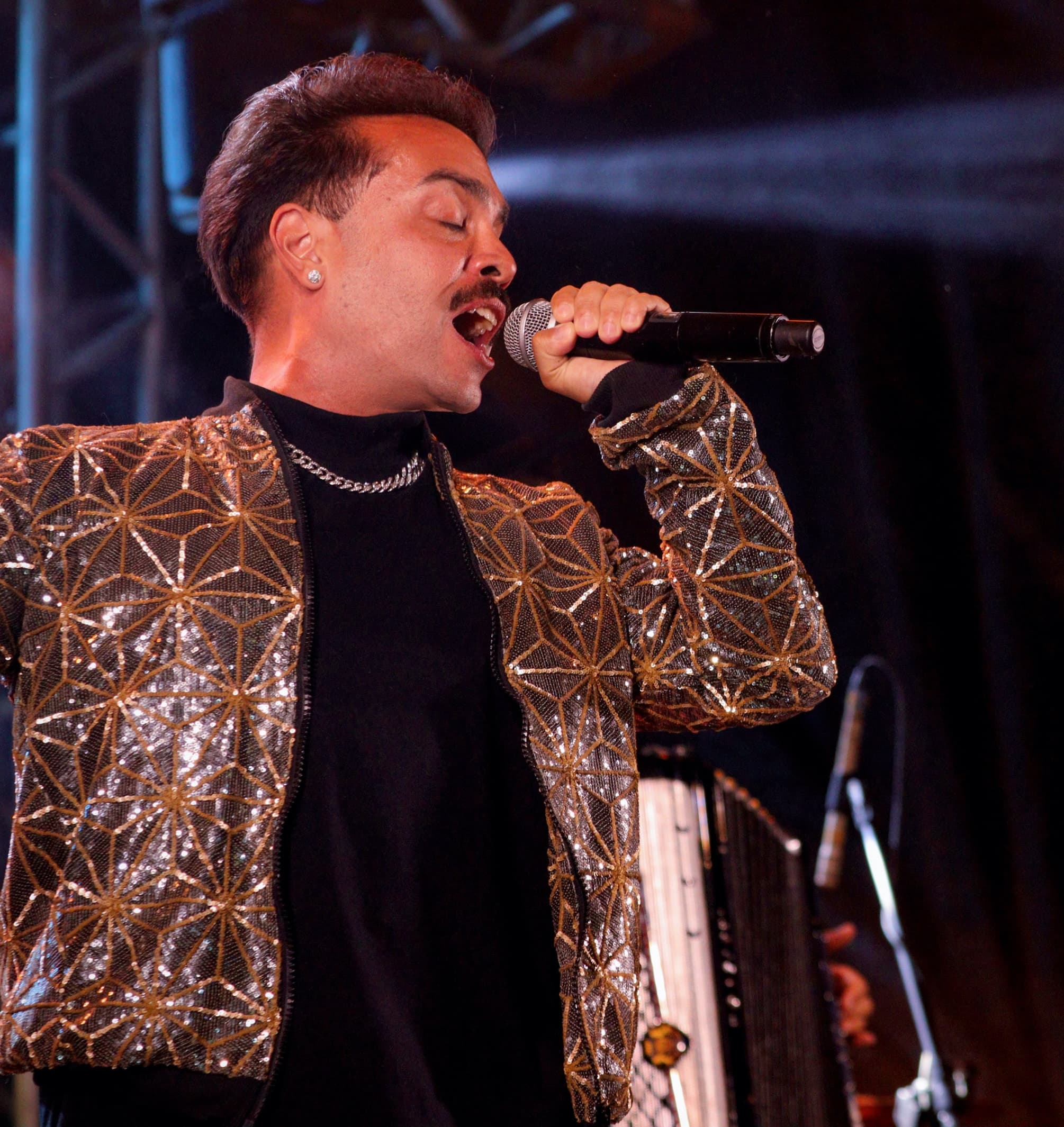 Vocalista de paetê dourado cantando ao microfone com os olhos fechados, sob luz de palco