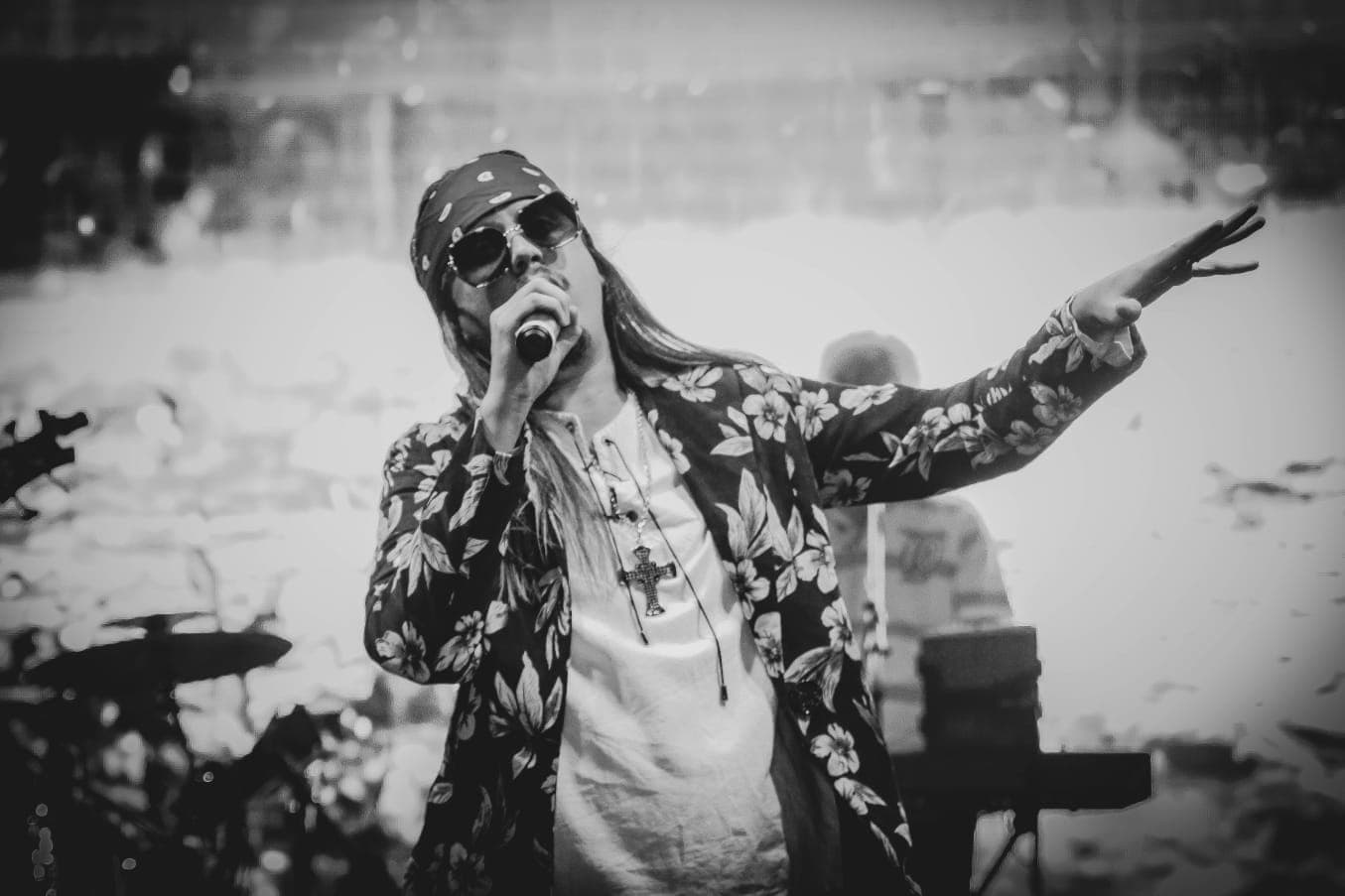 Vocalista de bandana e crucifixo cantando clássicos do rock com banda ao fundo
