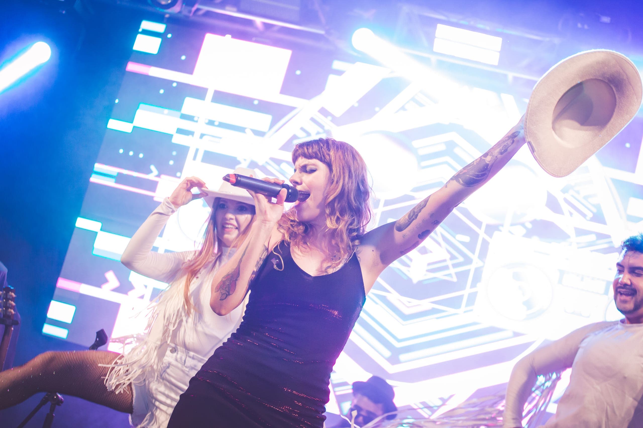 Cantora com chapéu country e bailarinos em movimento no palco